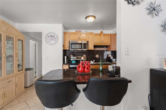 kitchen featuring dark countertops, backsplash, appliances with stainless steel finishes, a sink, and a kitchen breakfast bar