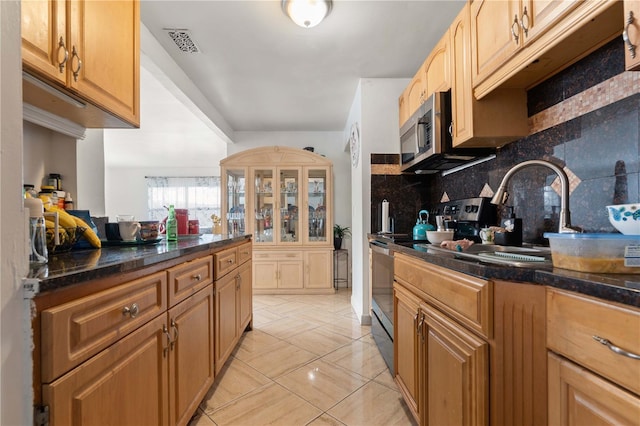 kitchen featuring tasteful backsplash, visible vents, stainless steel microwave, dark stone countertops, and a sink