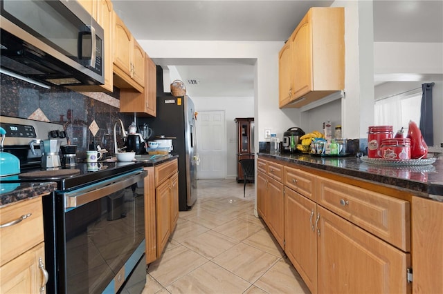 kitchen with appliances with stainless steel finishes, dark stone countertops, and tasteful backsplash