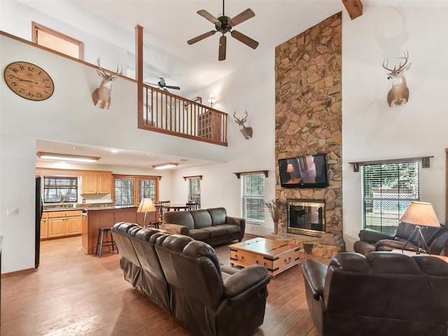 living area with a stone fireplace, ceiling fan, light wood-style flooring, and a towering ceiling