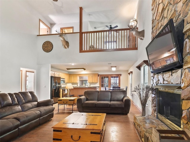 living room with a fireplace, a towering ceiling, hardwood / wood-style floors, and ceiling fan