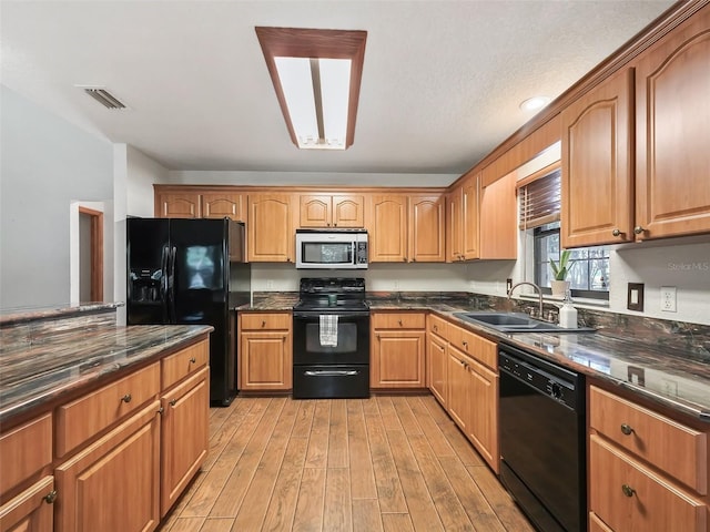 kitchen featuring a sink, visible vents, black appliances, light wood finished floors, and dark stone countertops