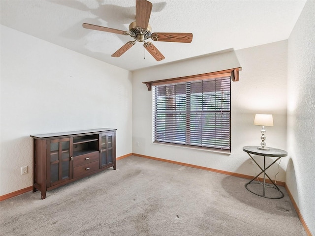 carpeted living room with ceiling fan, baseboards, and a textured wall