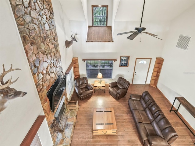 living room with a stone fireplace, a high ceiling, wood finished floors, and visible vents