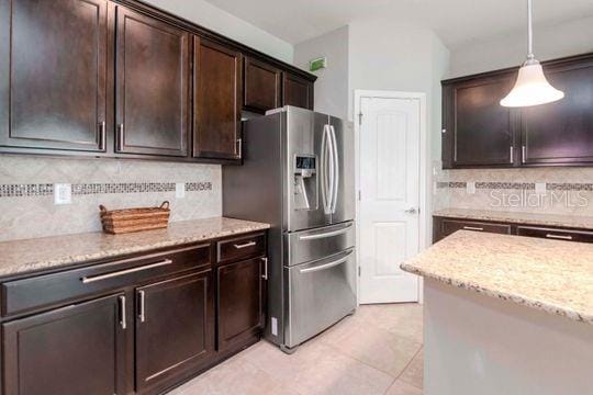 kitchen featuring light stone counters, decorative backsplash, dark brown cabinetry, decorative light fixtures, and stainless steel fridge