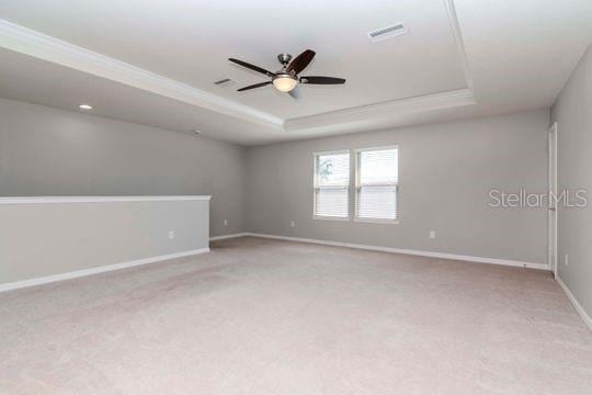 carpeted empty room with a raised ceiling, a ceiling fan, baseboards, and visible vents