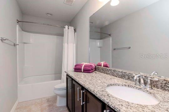 full bathroom with vanity, shower / bathtub combination with curtain, visible vents, tile patterned floors, and toilet