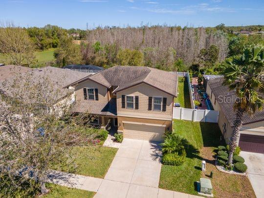 view of front facade featuring a forest view, a front lawn, fence, concrete driveway, and an attached garage