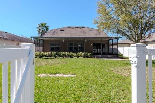 back of property featuring a lawn, a sunroom, ceiling fan, and fence