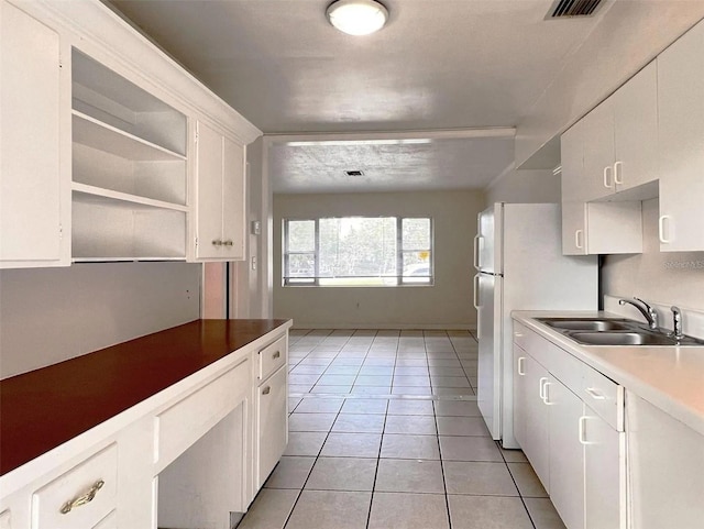 kitchen with light tile patterned floors, visible vents, white cabinets, freestanding refrigerator, and a sink