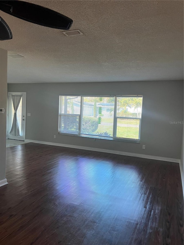 spare room with dark wood-type flooring, a textured ceiling, and baseboards