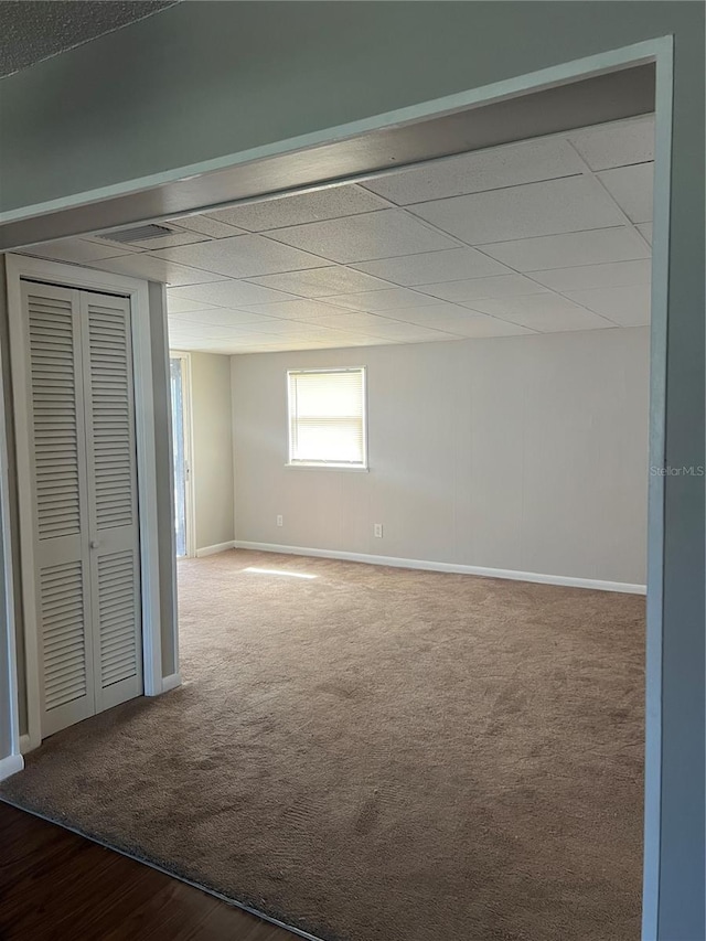 unfurnished bedroom with a paneled ceiling, carpet, baseboards, and a closet