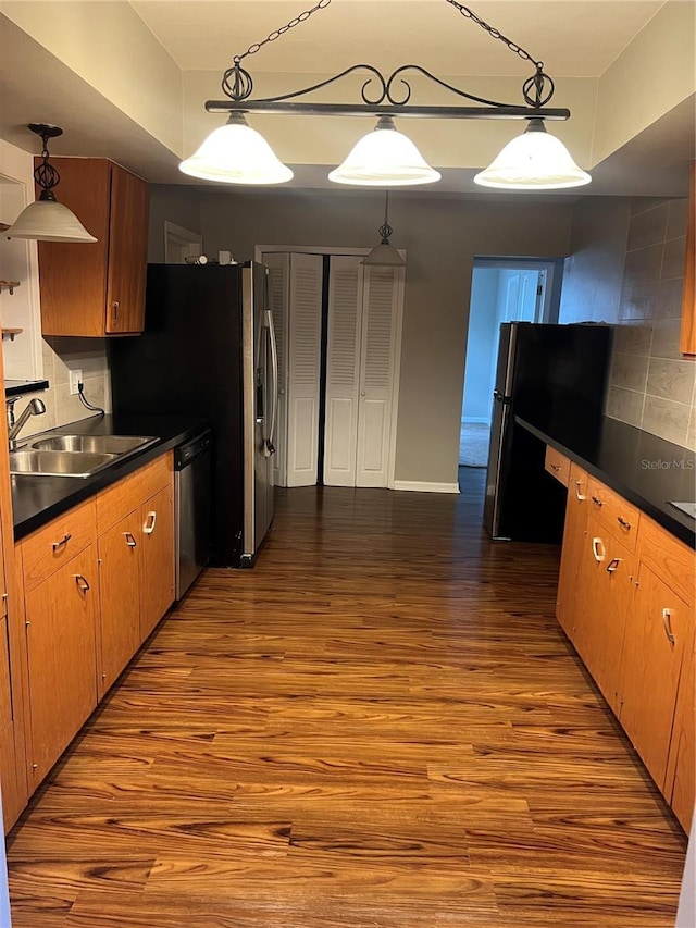 kitchen with dark countertops, freestanding refrigerator, a sink, wood finished floors, and dishwashing machine