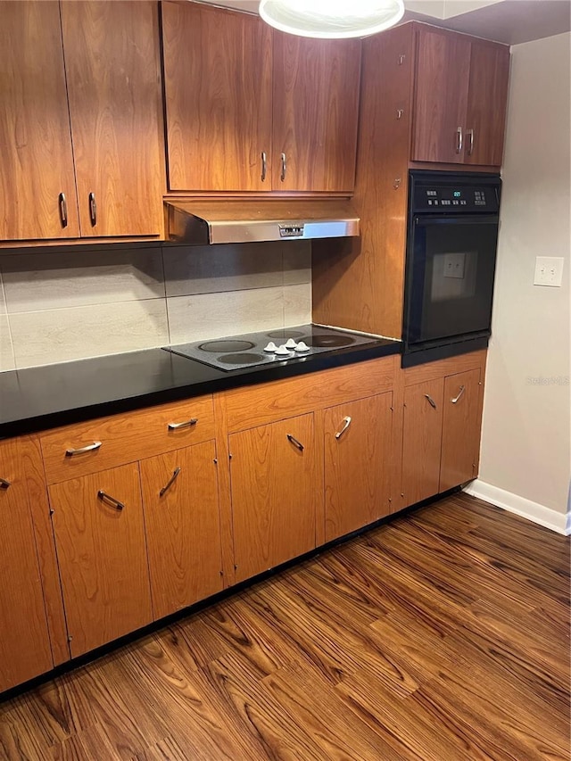 kitchen with black appliances, ventilation hood, dark countertops, and dark wood finished floors