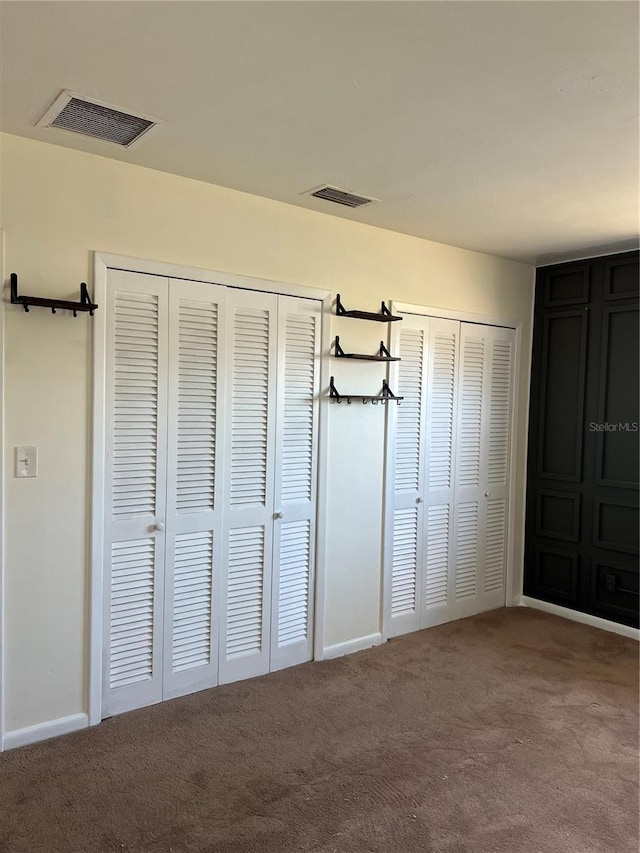 unfurnished bedroom with carpet floors, visible vents, and two closets