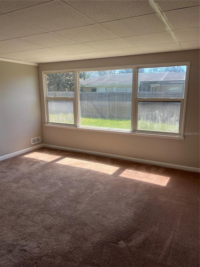 carpeted empty room featuring baseboards, visible vents, and a drop ceiling