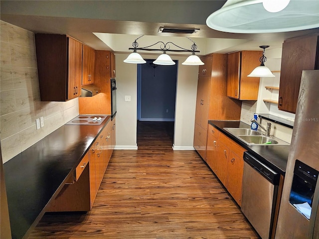 kitchen with a sink, dark countertops, appliances with stainless steel finishes, brown cabinetry, and dark wood-style flooring