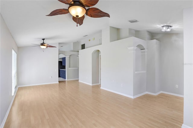 empty room with visible vents, lofted ceiling, arched walkways, ceiling fan, and light wood-style floors