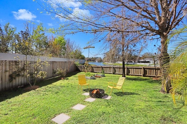 view of yard featuring a water view, a fire pit, and a fenced backyard