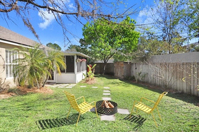 view of yard with a fire pit, a fenced backyard, and a sunroom