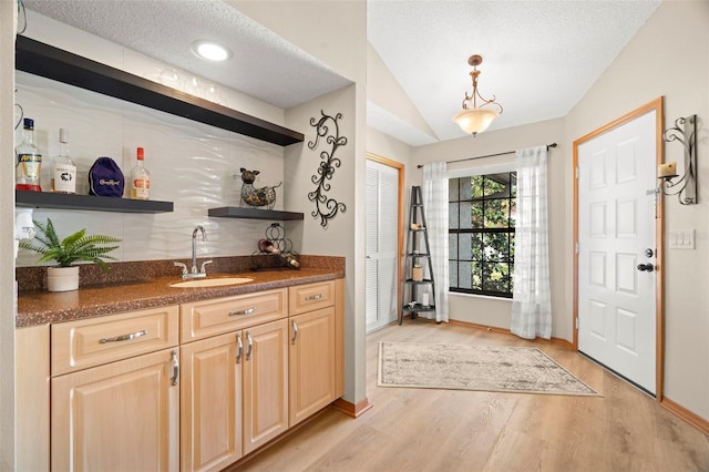 bar with indoor wet bar, lofted ceiling, light wood-style flooring, a sink, and a textured ceiling