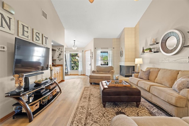 living room with a fireplace, visible vents, light wood-style flooring, high vaulted ceiling, and baseboards