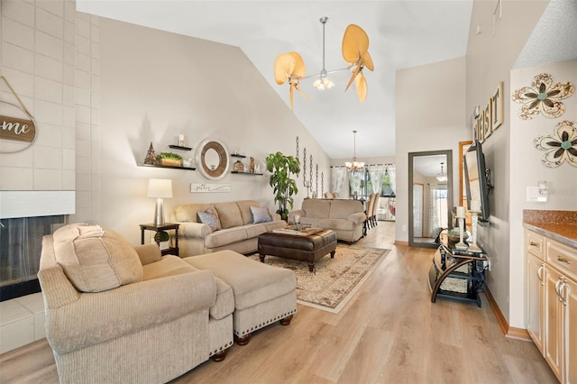 living area with a fireplace, an inviting chandelier, light wood-style floors, high vaulted ceiling, and baseboards