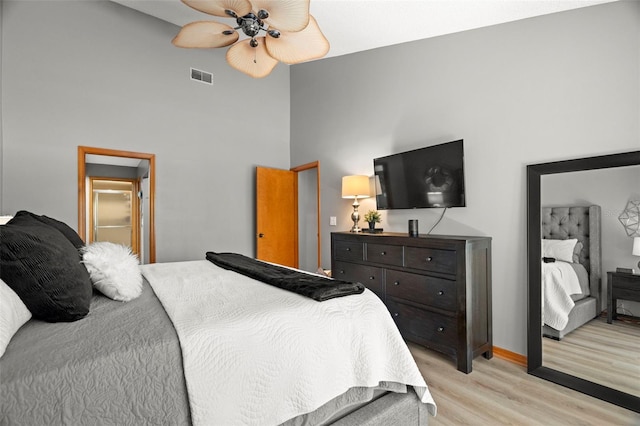 bedroom with baseboards, visible vents, a ceiling fan, a high ceiling, and light wood-style floors