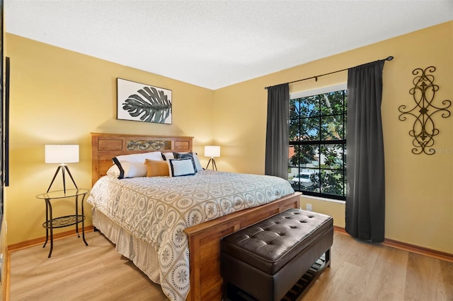 bedroom featuring light wood-type flooring, a textured ceiling, and baseboards