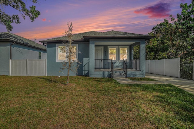 view of front of property with a shingled roof, fence, stucco siding, covered porch, and a yard