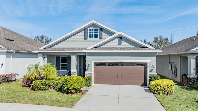 craftsman-style house with driveway, a shingled roof, an attached garage, a front yard, and stucco siding