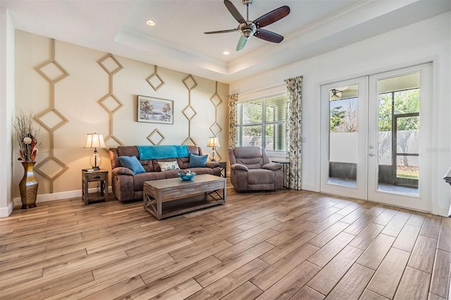 living area featuring french doors, a tray ceiling, light wood-style flooring, and baseboards