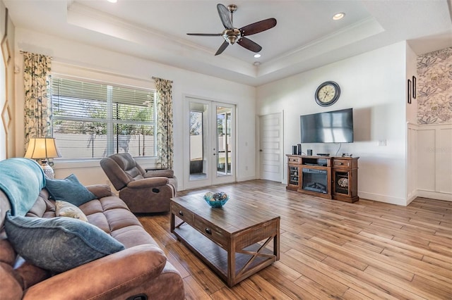 living room with light wood-style floors, a raised ceiling, and crown molding