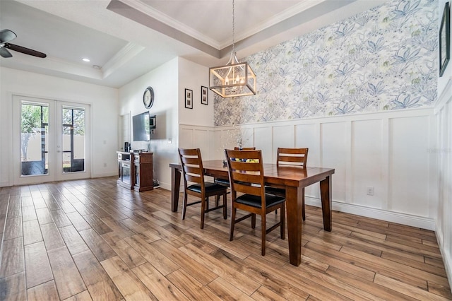 dining room featuring a wainscoted wall, a tray ceiling, light wood-type flooring, and ornamental molding