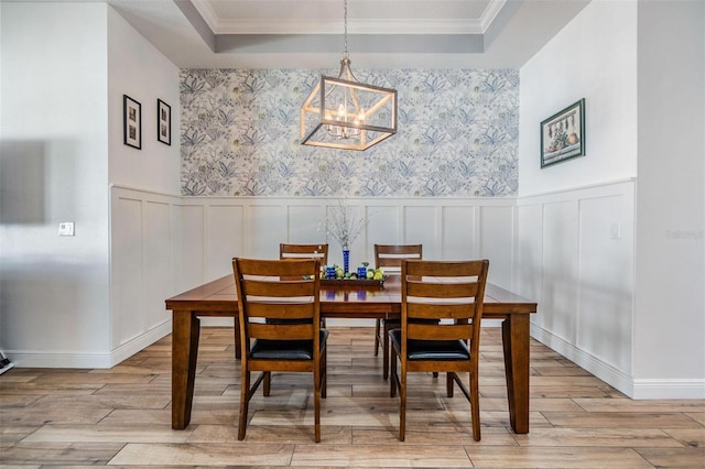 dining space featuring light wood-type flooring, a wainscoted wall, a chandelier, and a raised ceiling