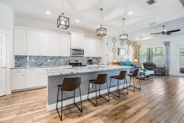 kitchen featuring visible vents, appliances with stainless steel finishes, open floor plan, a breakfast bar area, and light wood-style floors