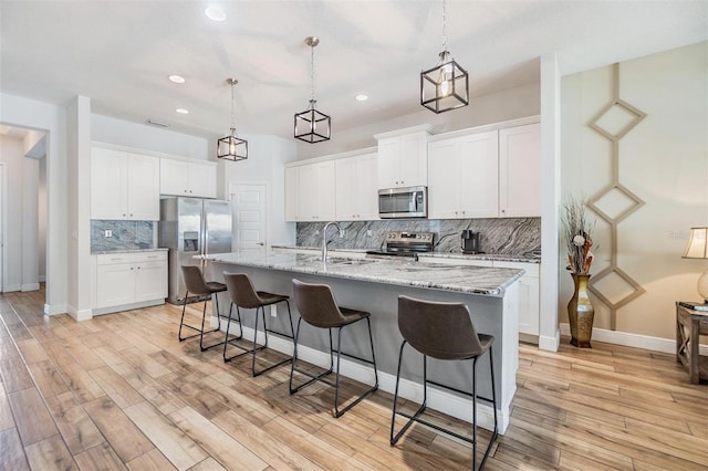 kitchen featuring a breakfast bar, stainless steel appliances, light wood-style flooring, white cabinets, and a sink