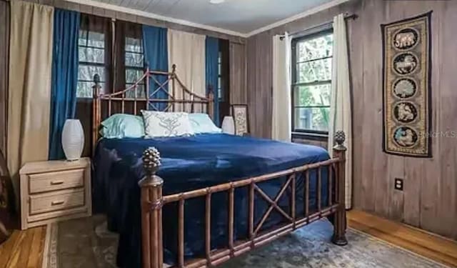 bedroom with crown molding, wooden walls, and wood finished floors