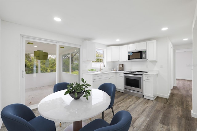 kitchen featuring white cabinets, appliances with stainless steel finishes, wood finished floors, light countertops, and a sink