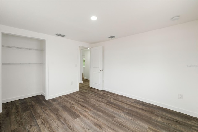 unfurnished bedroom with dark wood-type flooring, a closet, visible vents, and baseboards