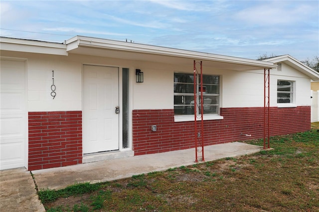 doorway to property featuring a garage and brick siding