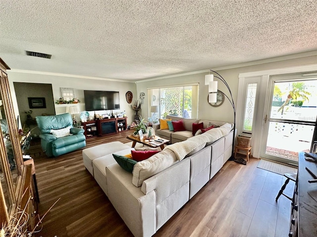 living room featuring crown molding, a textured ceiling, visible vents, and wood finished floors