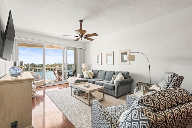 3805 Gulf Blvd Unit 404, St Pete Beach, FL 33706 - living area featuring ceiling fan, a water view, wood finished floors, a textured ceiling, and a textured wall
