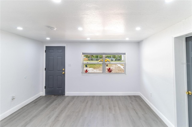 spare room with recessed lighting, baseboards, a textured ceiling, and light wood finished floors