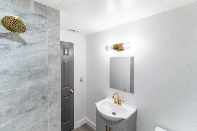 full bath featuring visible vents, tiled shower, and vanity