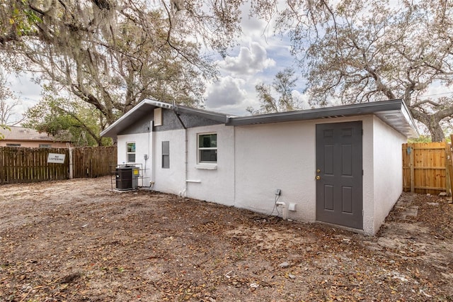 back of property with central AC, fence, and stucco siding