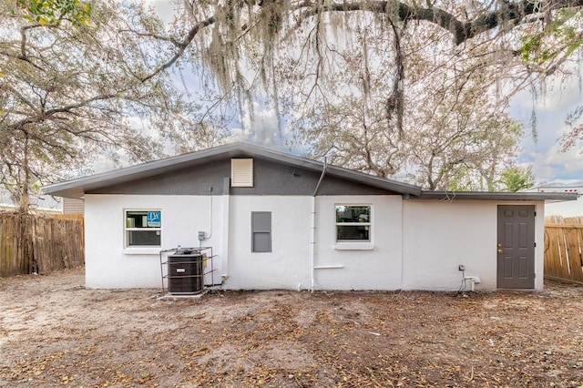 back of house featuring central AC unit, fence, and stucco siding