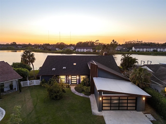 view of front of house with concrete driveway, a water view, an attached garage, fence, and a front yard