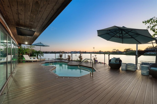 pool at dusk with a deck with water view and a fenced in pool