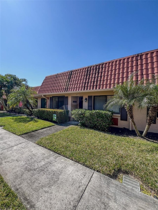 view of front of property featuring mansard roof, a front yard, a tile roof, and stucco siding